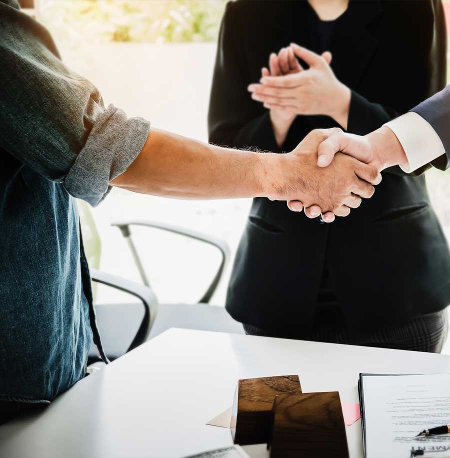 Two men shaking hands over a table while a woman applauds behind them